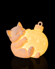 Gatinho branco dormindo abraçado a uma bola de Natal iluminada por dentro